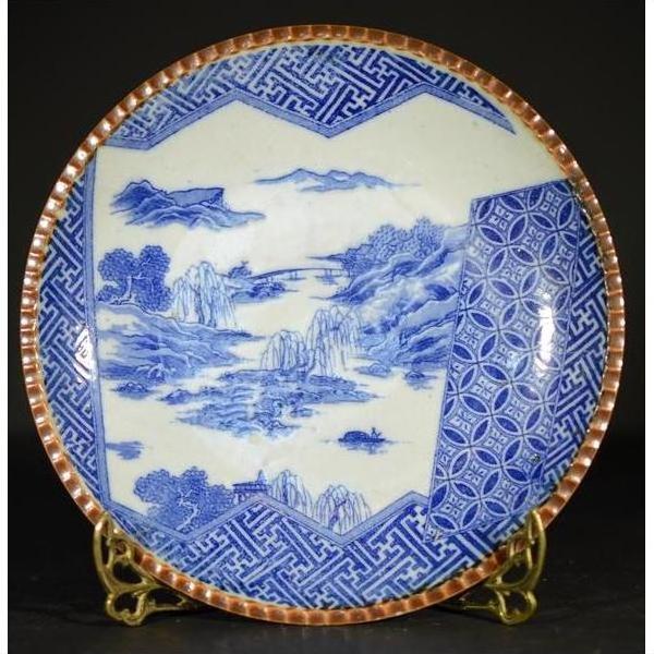 Blue and white ceramic Igezara transferware plate with landscape and geometric rim, on metal stand.