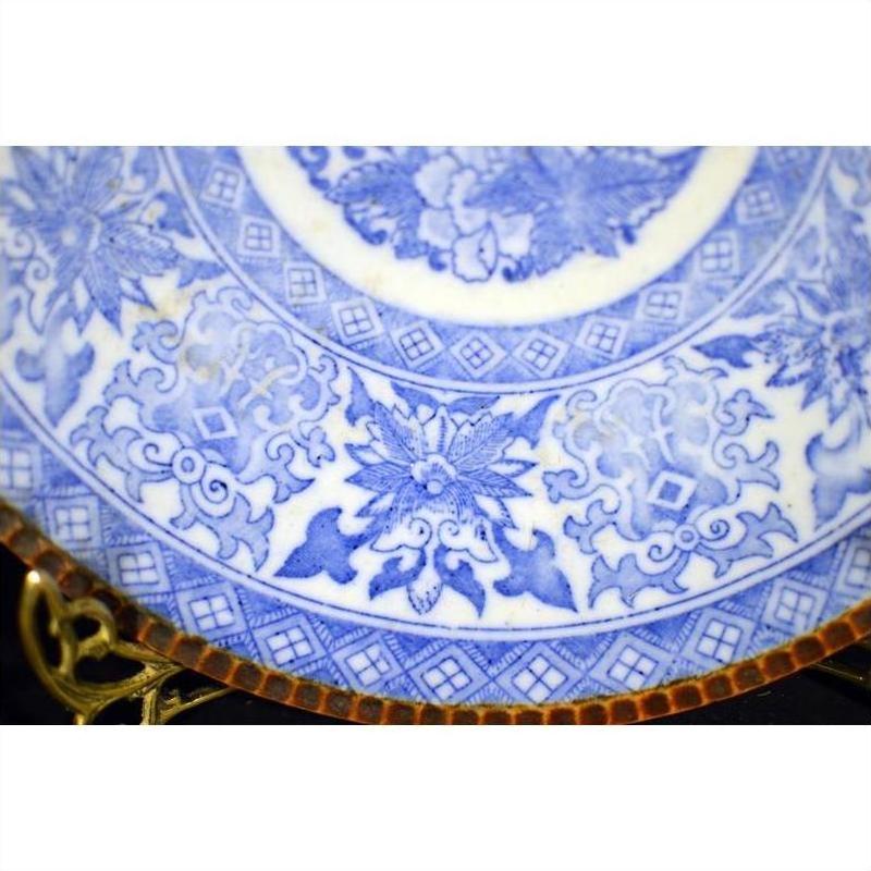 Close-up of blue and white ceramic Japanese Igezara transferware plate with floral and geometric designs on display stand.