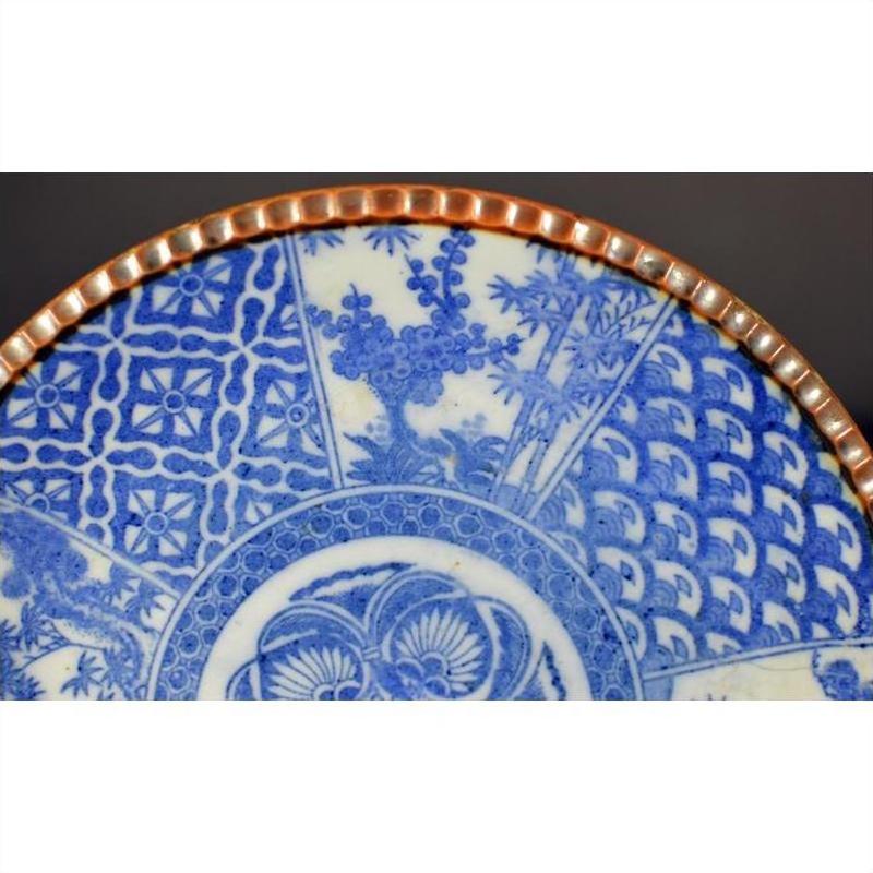 Close-up of blue and white porcelain Japanese Igezara plate with transferware patterns and a scalloped brown edge.