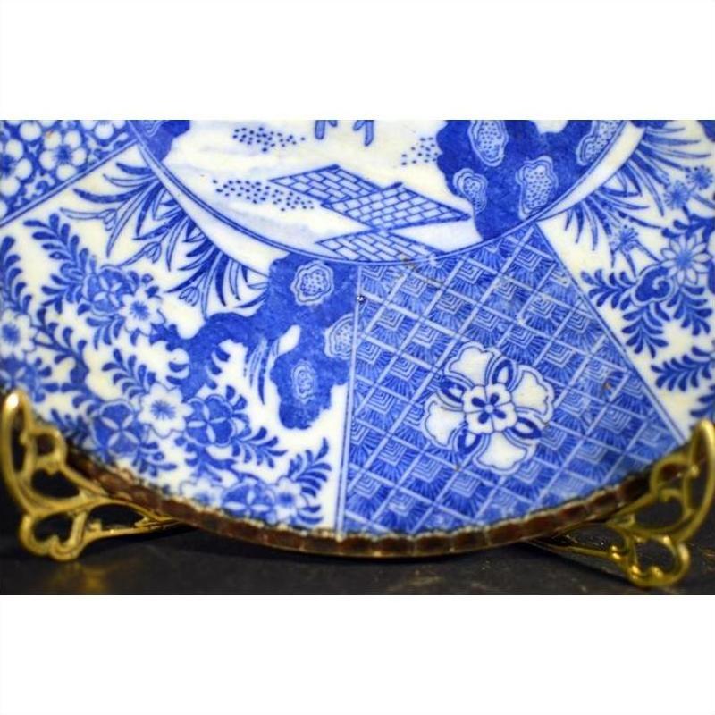 White and blue porcelain plate with floral and geometric designs on a gold stand.
