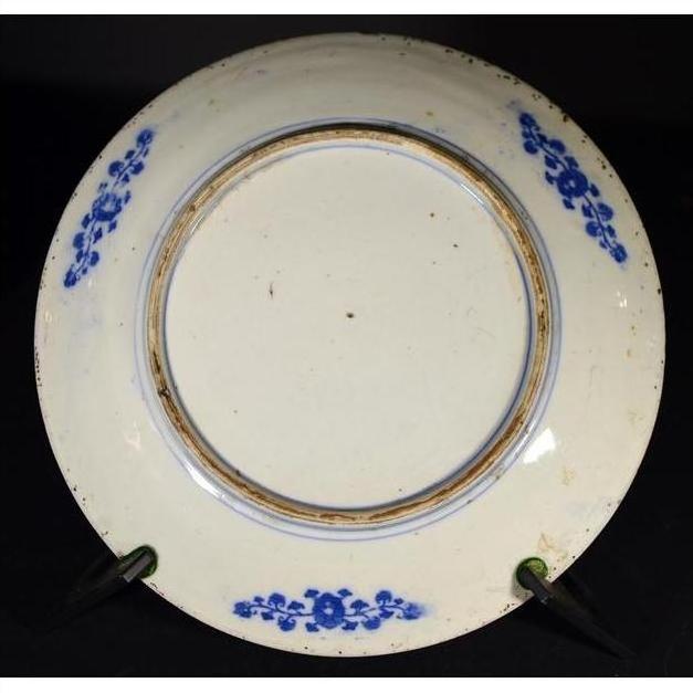 Blue and white porcelain plate with floral rim on black stand, dark background.