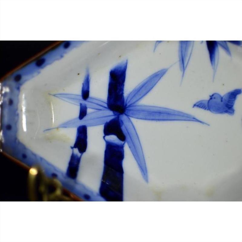 White and blue porcelain Imari bowl with hand painted bamboo, leaves, and small bird design, close-up view.