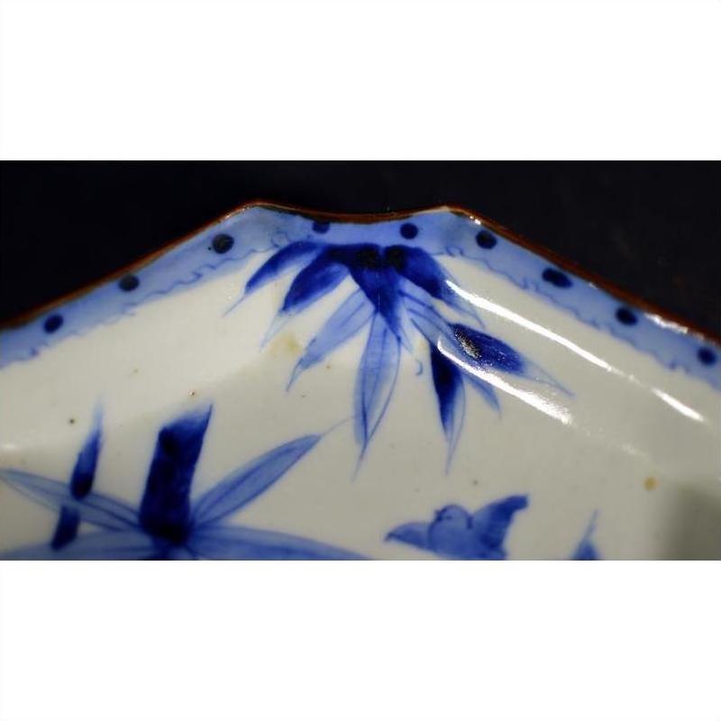 Close-up of blue and white porcelain Japanese Imari bowl with hand-painted floral designs and scalloped brown-edged rim.