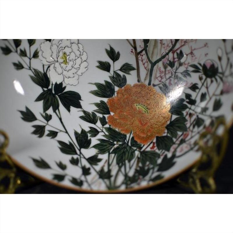Close-up of a porcelain Kutani bowl, hand painted with white and orange flowers and green leaves, antique style.