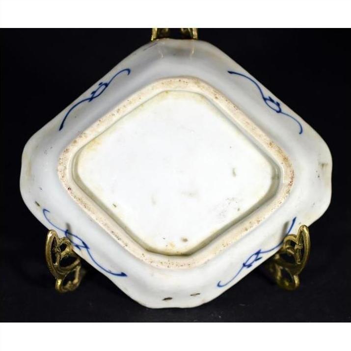 Close-up of an antique Japanese Kutani hand painted porcelain dish base on a metal stand against a dark background.