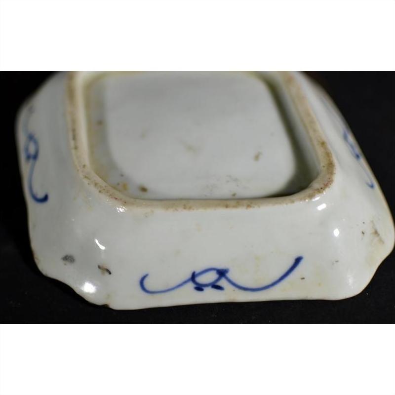 Close-up of antique Japanese Kutani porcelain dish with blue hand-painted scrolls on an aged white ceramic base.
