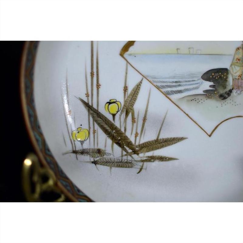 Close-up of an antique Japanese Kutani porcelain plate with hand painted yellow fruit and brown-green leaves by water.