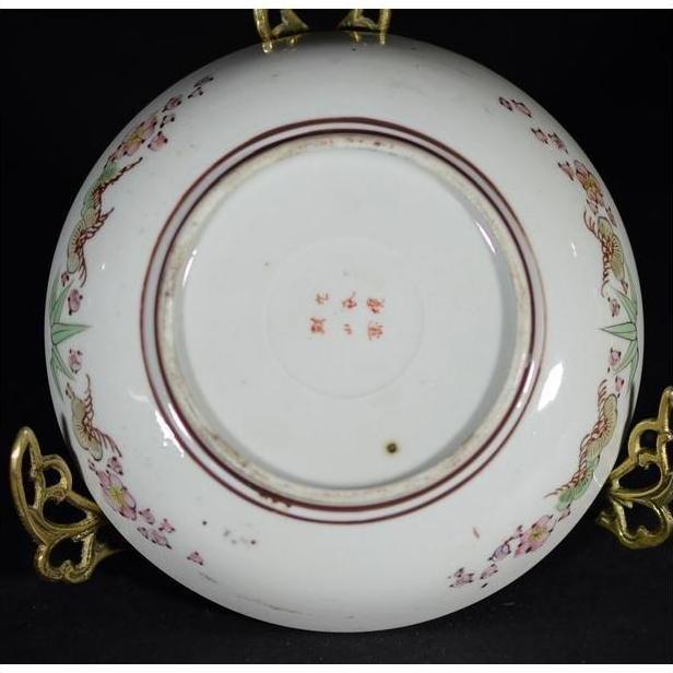 Close-up of the base of an antique Japanese Kutani porcelain plate with floral designs and bold red characters.
