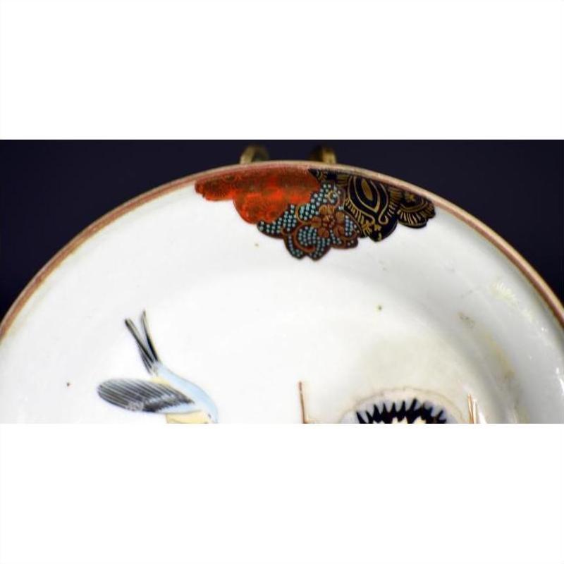 Close-up of antique hand painted Japanese Kutani porcelain plate with bird and floral designs on dark background.