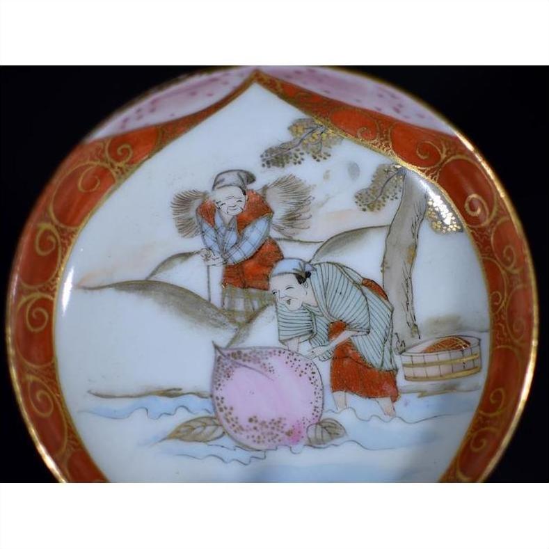 Close-up of an antique Japanese Satsuma porcelain plate with two figures by a river under a tree, one holding a basket.