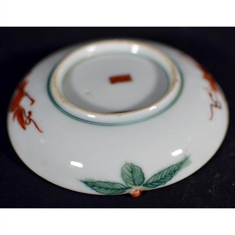 White porcelain plate with green leaf design and red mark, antique Japanese Satsuma, close-up on plain background.