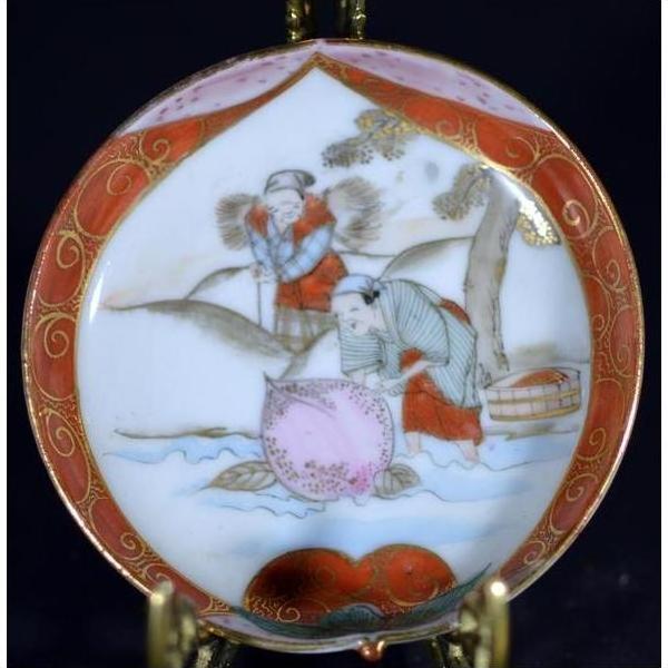 Close-up of vibrant red and gold hand-painted ceramic Japanese Satsuma plate with two figures by a river.