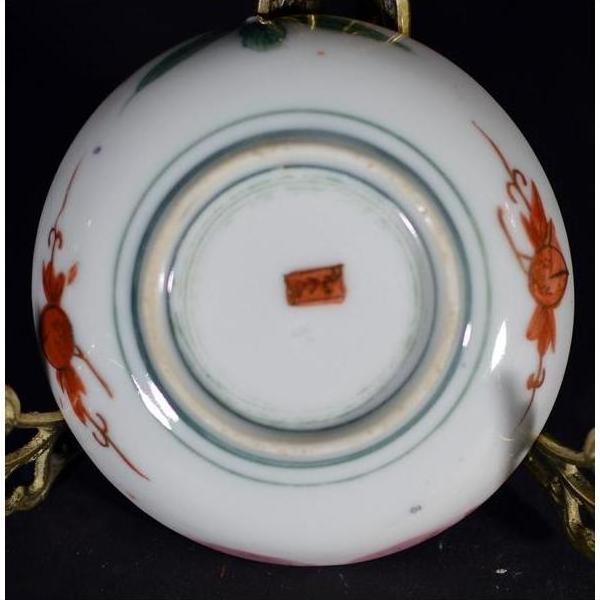 Close-up of underside of antique Japanese Satsuma porcelain plate with red floral designs and small red center mark.