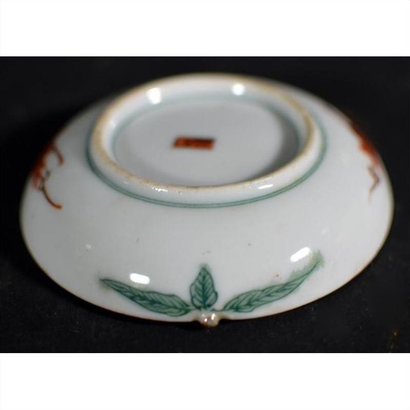 Close-up of the underside of a ceramic Satsuma plate with green leaf motif and small red square mark at the center.