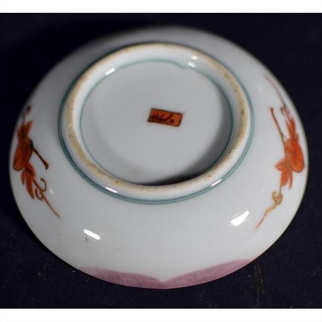 Red ceramic plate with hand painted floral designs and red base mark, displayed on a dark background.