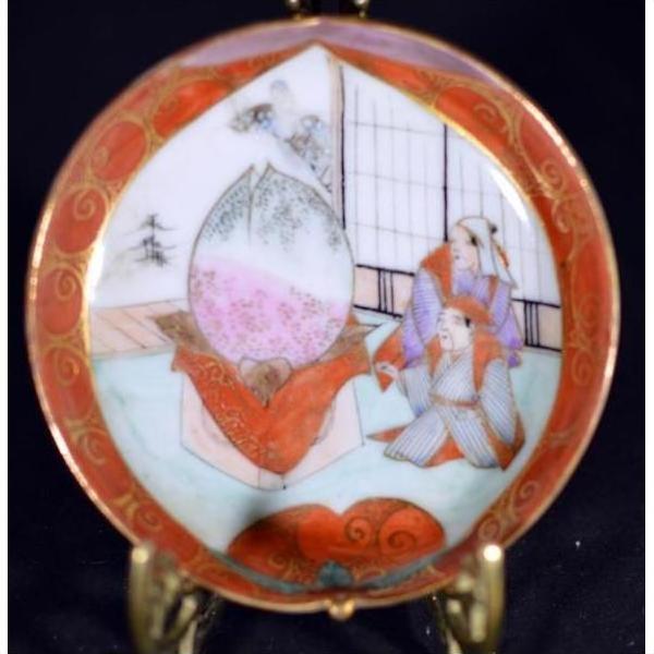 Close-up of antique Japanese Satsuma porcelain plate with red border, figures in traditional dress opening a giant peach.
