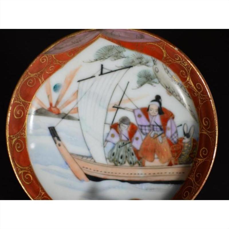 Close-up of an antique Japanese Satsuma ceramic plate with red border, painted sailboat figures, and scenic landscape.