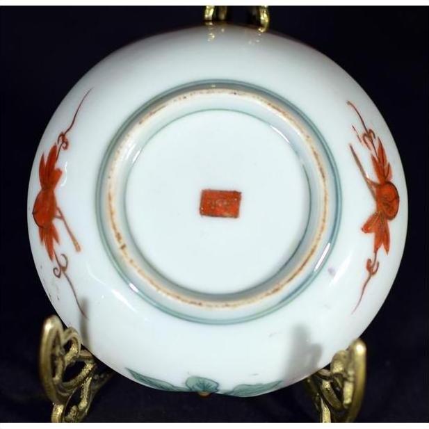 Close-up of bottom of antique Japanese Satsuma porcelain plate with red floral designs and red square mark on stand.
