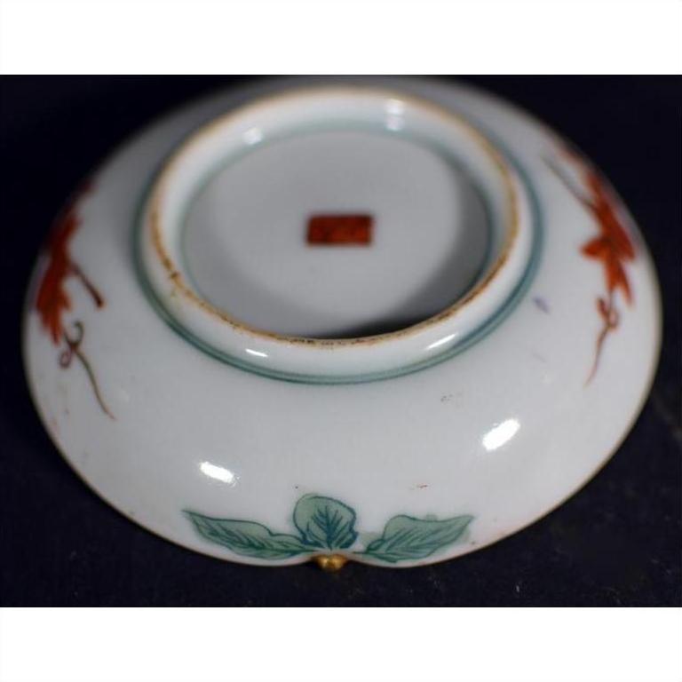 Close-up of an antique Japanese Satsuma porcelain plate with green leaf designs and a red mark on the base.