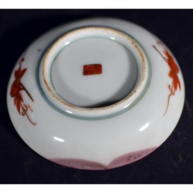 Close-up of an antique Japanese Satsuma porcelain plate with red floral designs and a red stamp.
