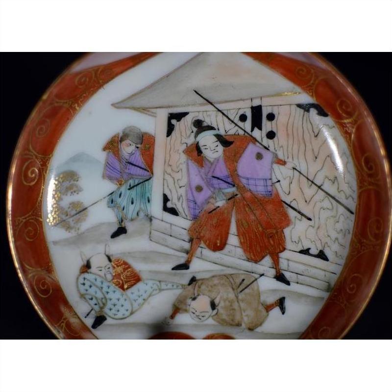 Colorful ceramic Satsuma plate with samurai in robes and spears battling near a building, two figures lying nearby.