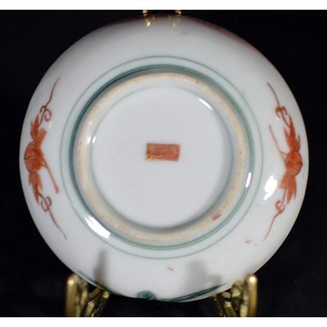 Close-up of the underside of an antique Japanese Satsuma porcelain plate with red hand-painted designs and a red stamp.