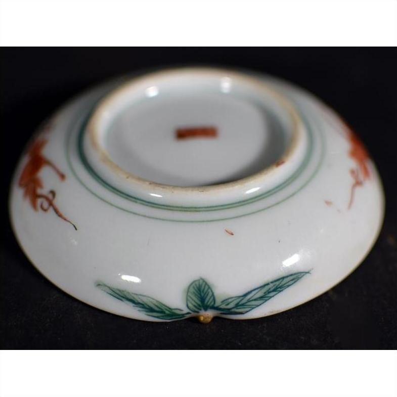 Close-up of an antique Japanese Satsuma porcelain plate with green leaves and red designs on a dark surface.