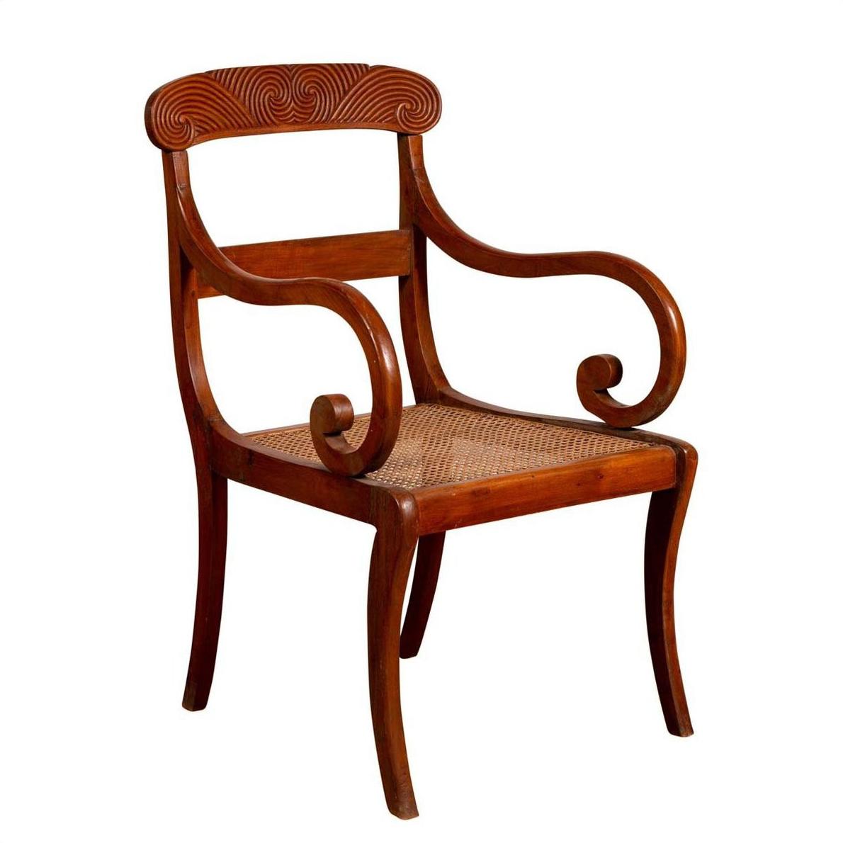 Brown wooden and rattan armchair with carved back and curving arms, antique Javanese style, indoor setting.