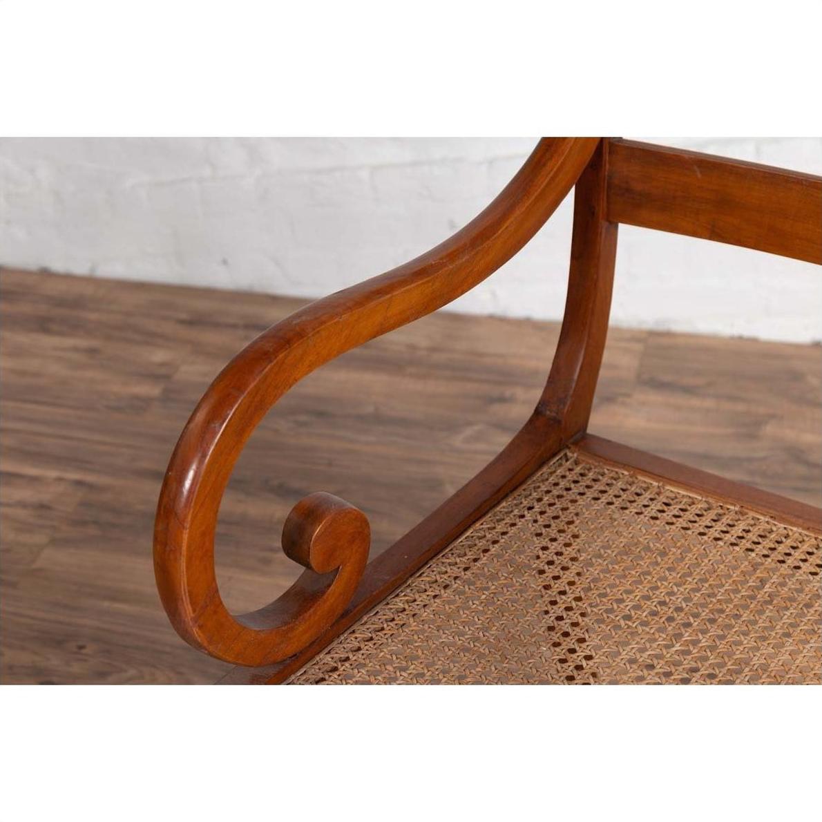 Brown wood and rattan armchair with carved back and curved arms on a wooden floor.