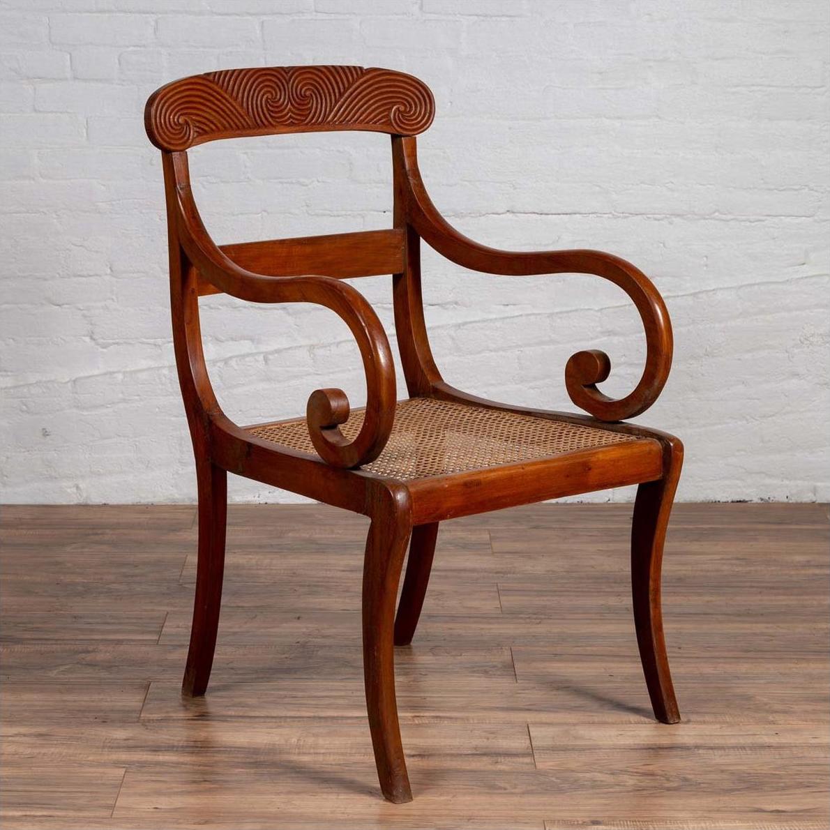 Brown wood and rattan armchair with carved back and curving arms on a wooden floor indoors.