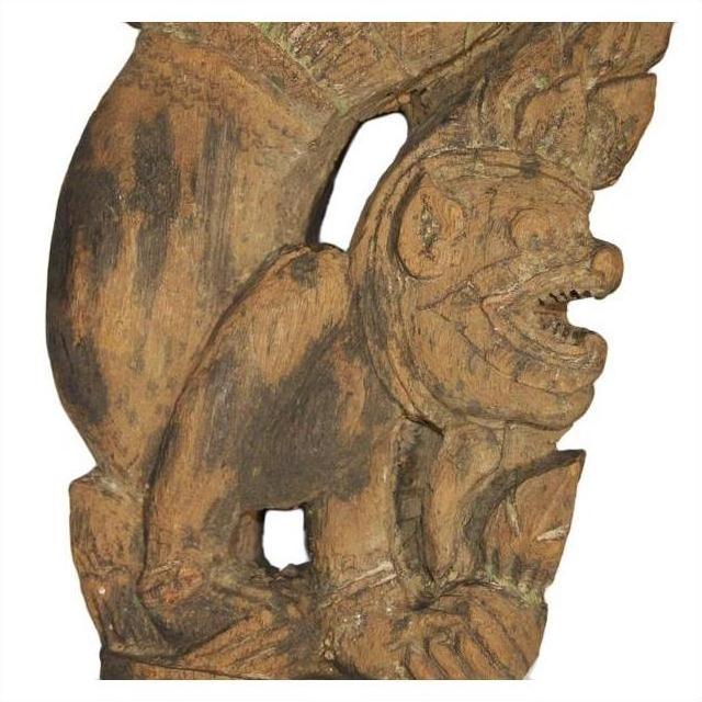 Brown wood Burmese temple carving, mirrored guardian relief with intricate headgear and expressive details, close-up.