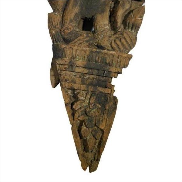 Brown wood temple carving, mirrored Burmese guardian relief with stylized headgear, floral and geometric motifs.