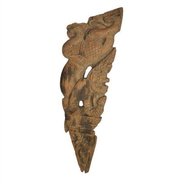 Brown wood temple carving, mirrored guardian relief with stylized headgear and intricate patterns, close-up view.