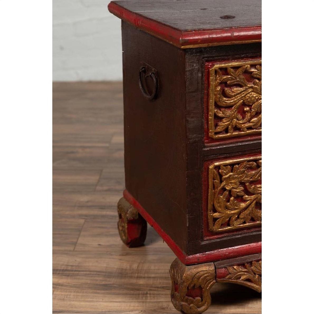 Brown hand-carved wooden blanket chest with gilt accents, metal handle, and decorative legs on a wooden floor.