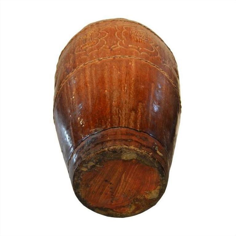 Brown wooden Martaban water jar with visible grain and carved floral patterns, bottom view.
