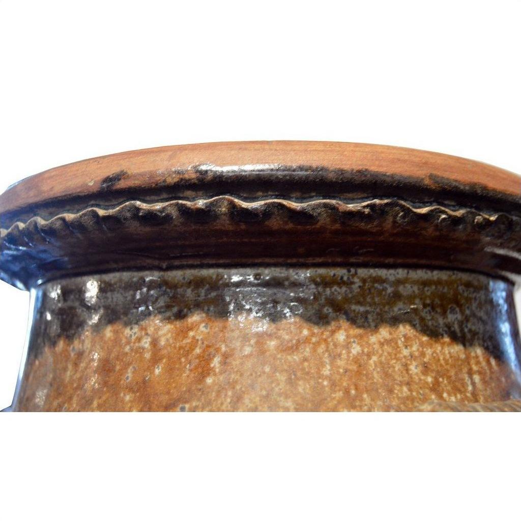 Close-up of brown ceramic rim and upper edge of antique Martaban water jar with wavy decorative pattern.