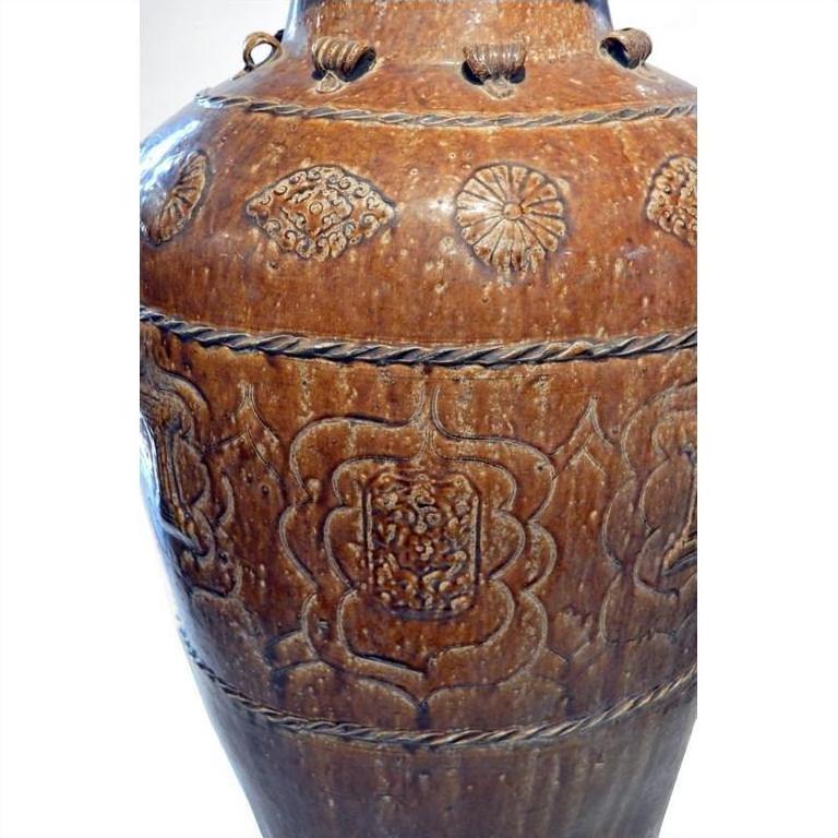 Brown ceramic Martaban water jar with floral patterns and textured bands, close-up view.