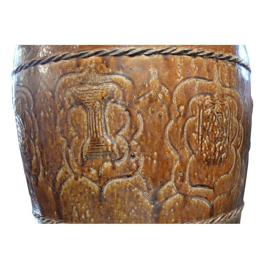 Close-up of brown ceramic jar with embossed floral and pillar patterns in geometric shapes.