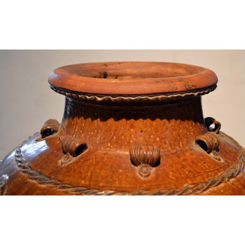 Close-up of a brown ceramic water jar with textured patterns and sturdy rim handles.