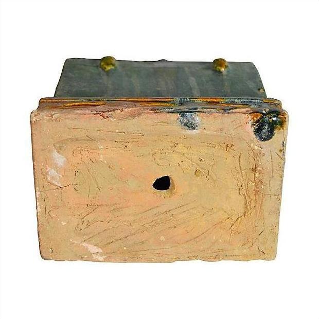 Close-up of a brown clay miniature Chinese treasure chest with a weathered finish, metal plate top, and two round bolt accents.