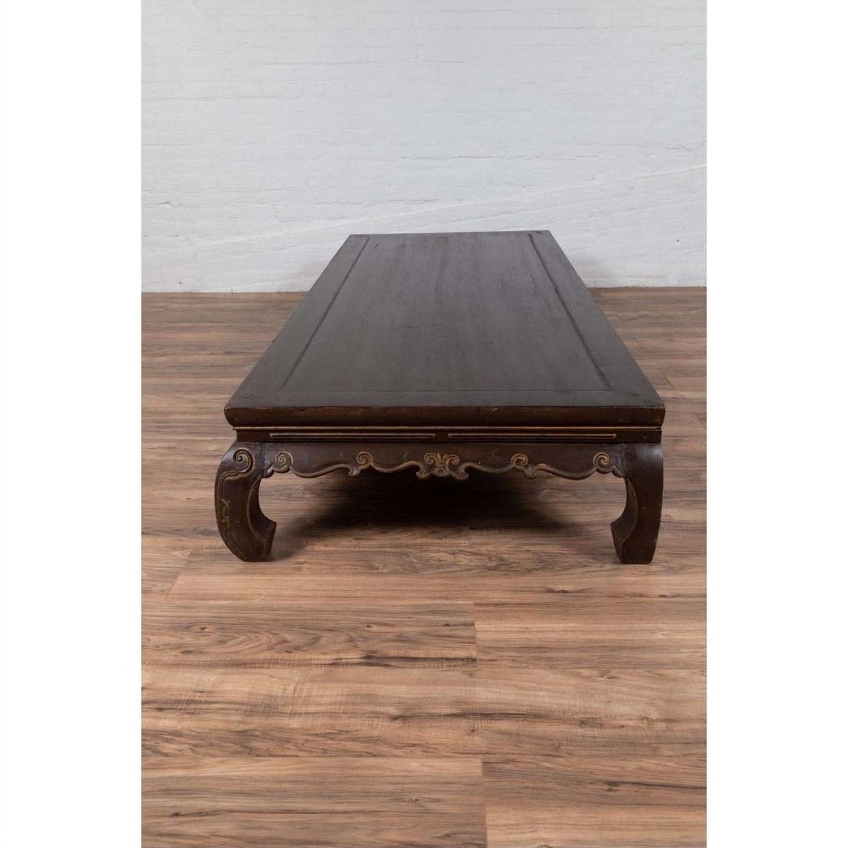Brown wood Ming Dynasty style Kang opium bed on a brown wood floor, set against a plain white wall indoors.
