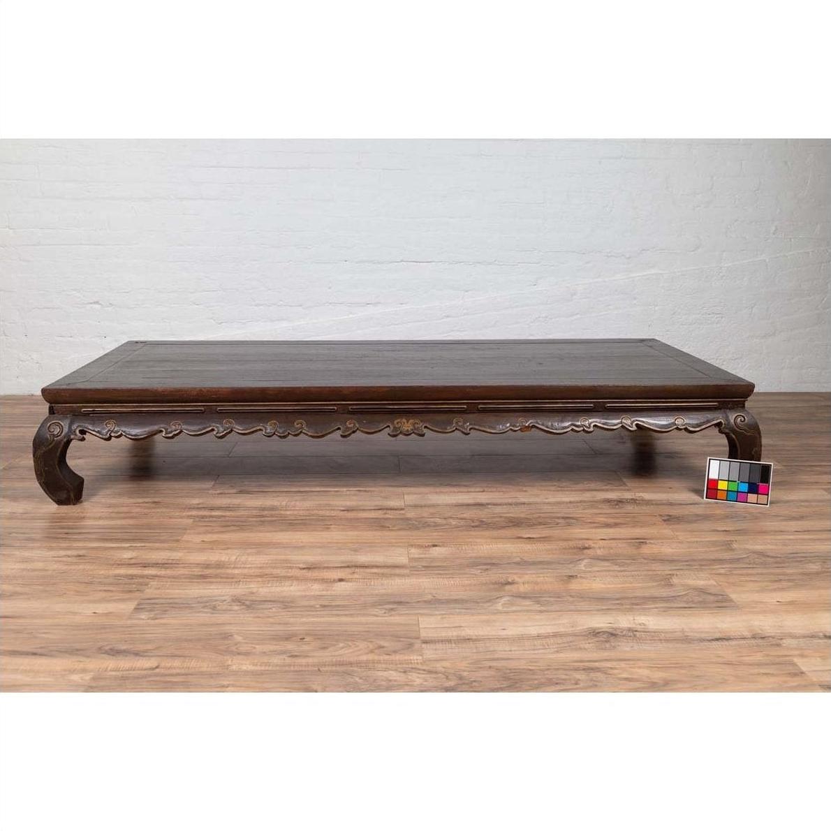 Dark wood Ming Dynasty style Kang opium bed with hand-carved legs on a wood floor next to a color calibration card.