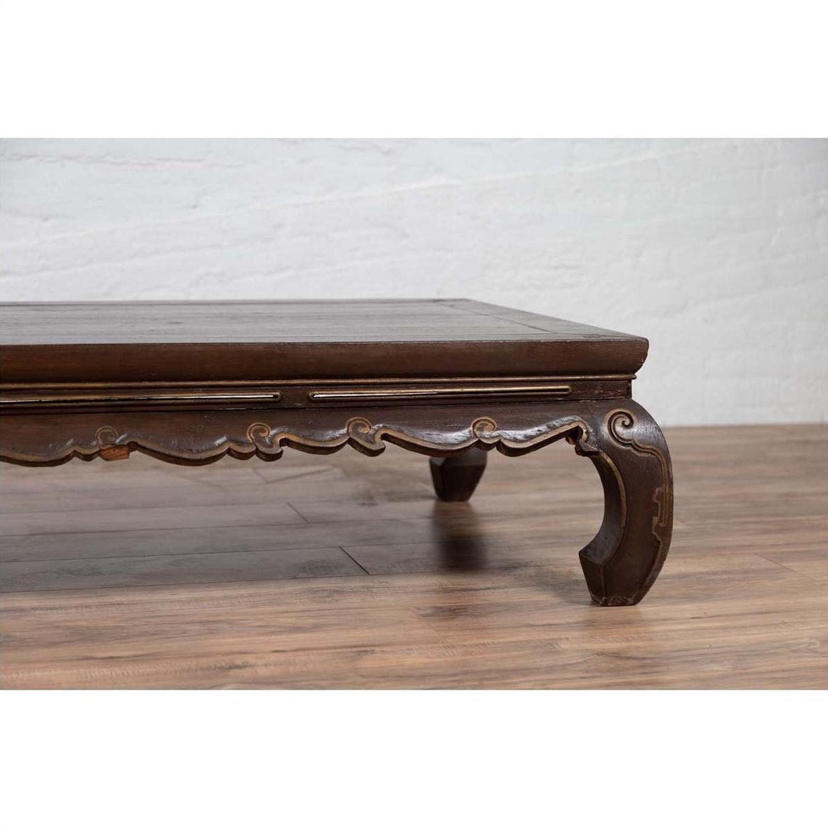 Dark wood low opium bed with curved legs on hardwood floor against white brick wall indoors.