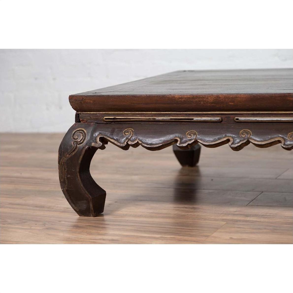 Close-up of dark wood Northern Chinese Ming Dynasty style bed with hand-carved frieze and scalloped apron indoors.