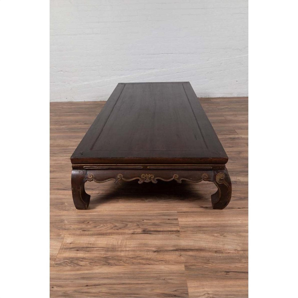 Wooden Northern Chinese Ming style opium bed with hand-carved legs on a wooden floor against a white wall indoors.