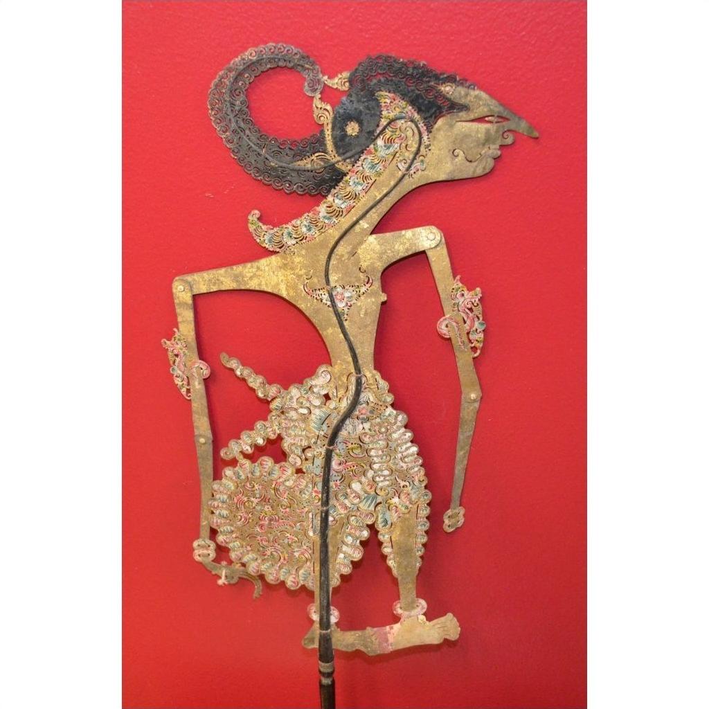Red background, leather antique shadow puppet with intricate Indonesian patterns, close-up view.