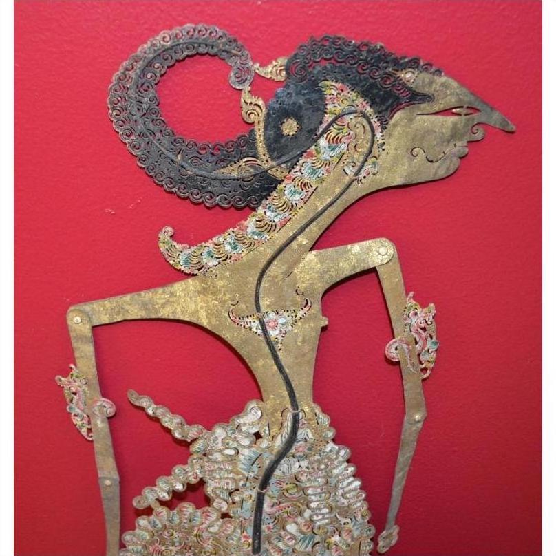 Close-up of antique leather shadow puppet with intricate carvings on a vibrant red background.