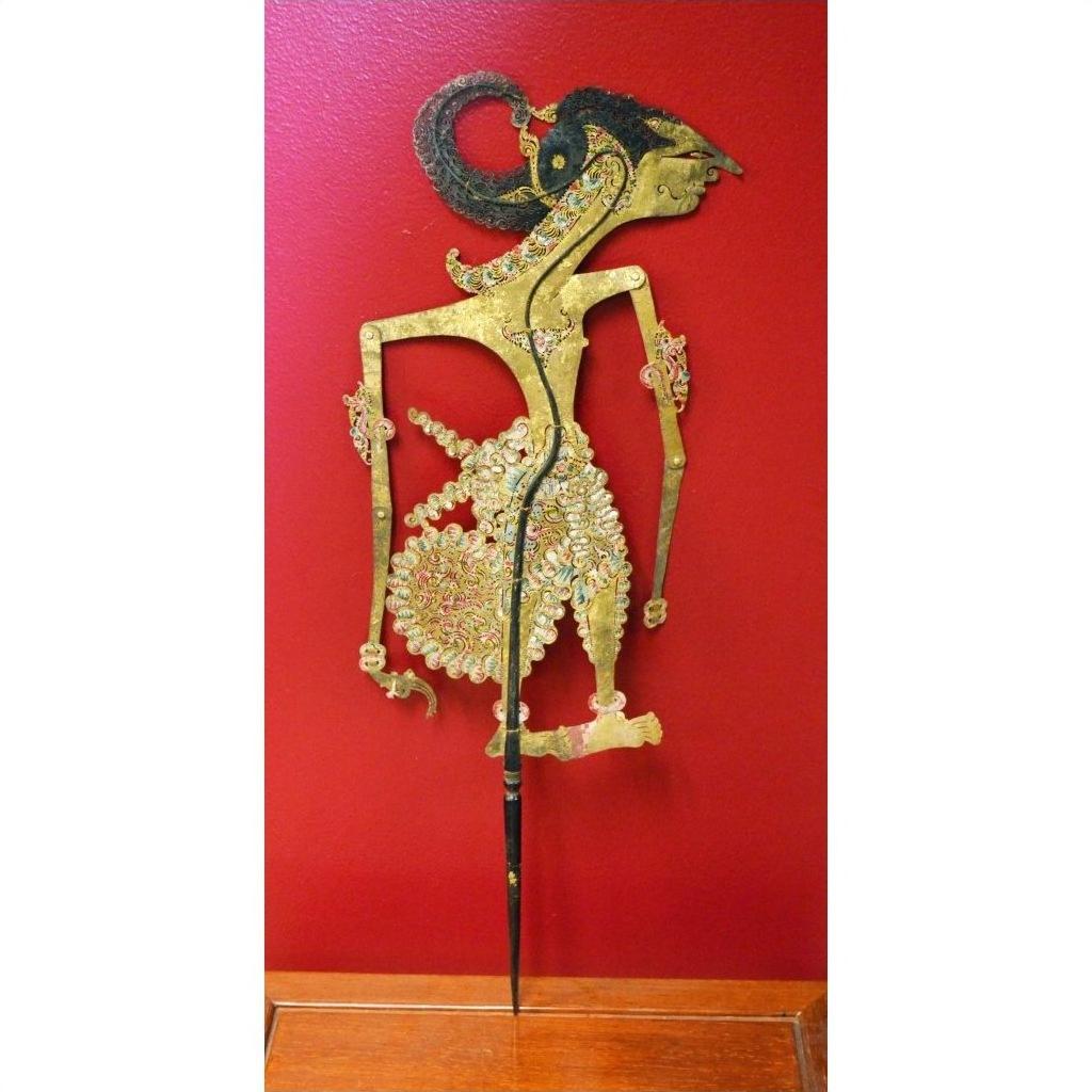 Gold and red leather Indonesian shadow puppet, close-up, displayed against a vibrant red background.