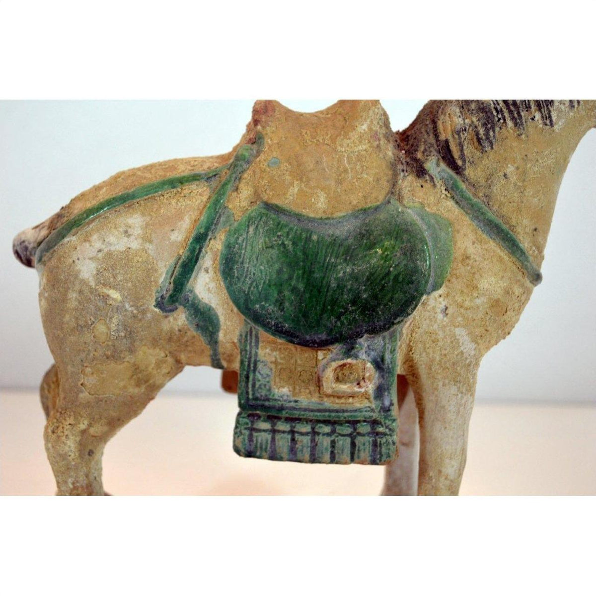 Glazed terracotta horse with green saddle, side view, Ming Dynasty style against plain background.