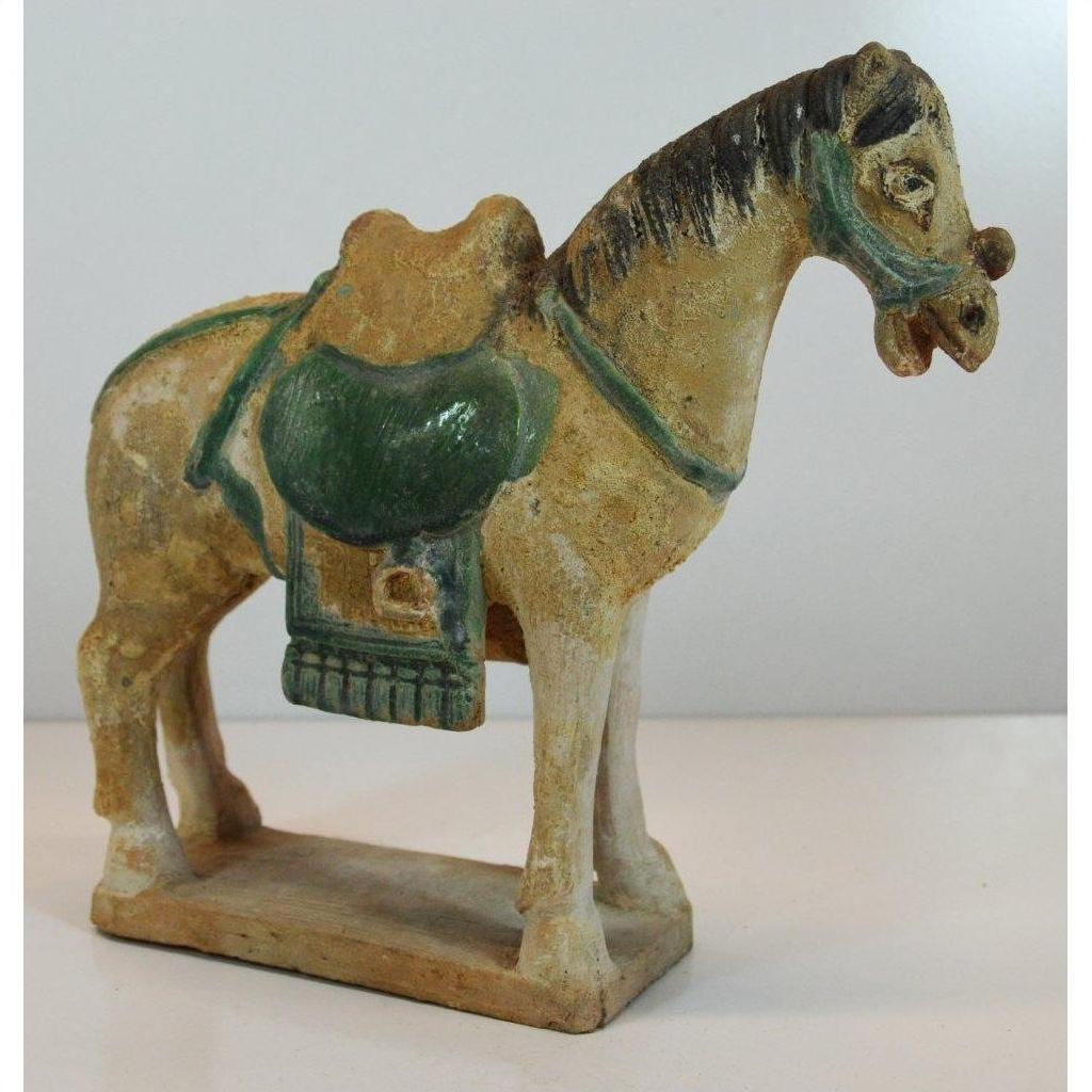 Glazed terracotta horse with green saddle from Ming Dynasty on rectangular base, close-up view.